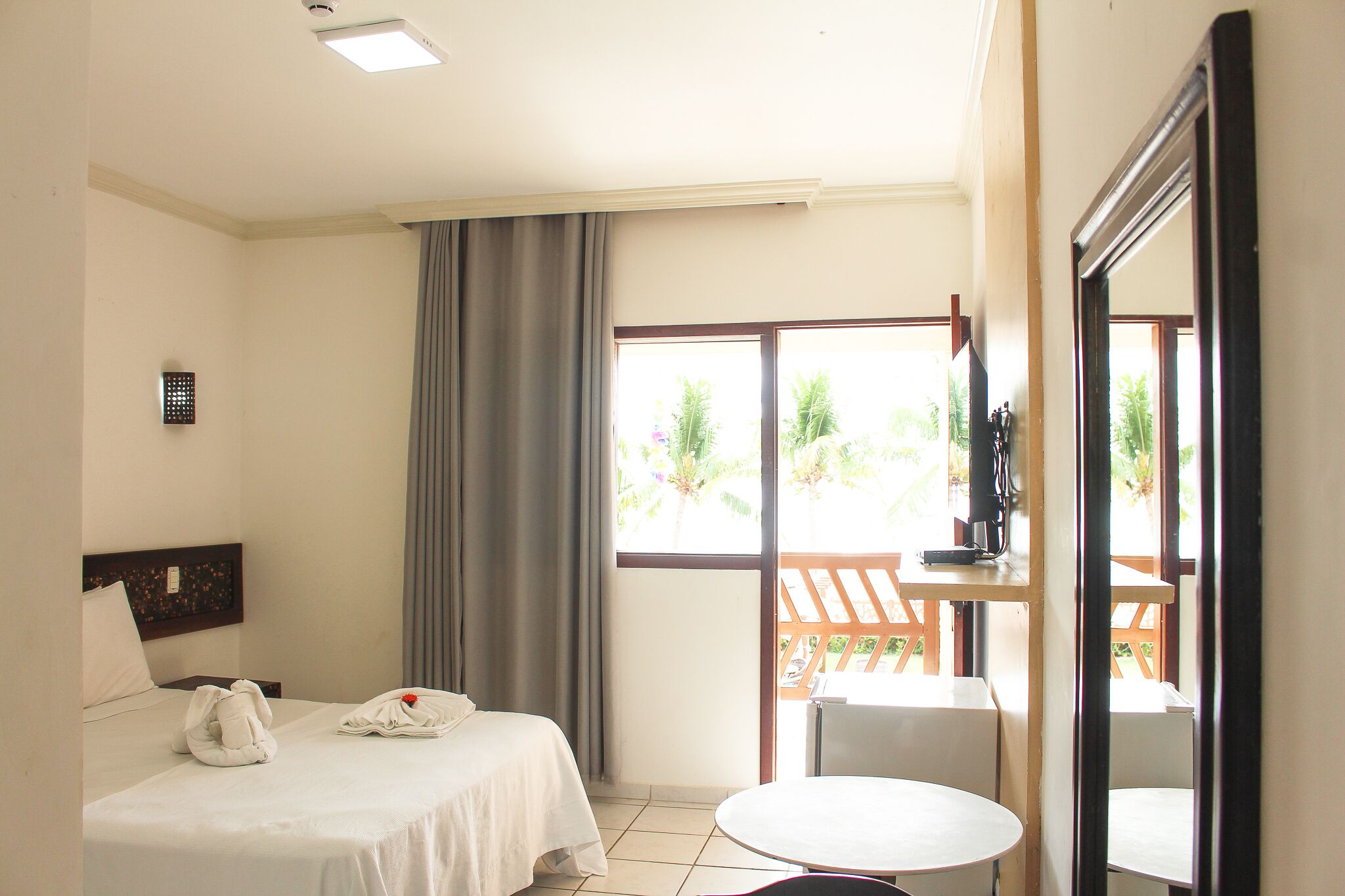 Habitación de hotel con cama, una mesita, una silla, ventana con cortinas y vistas al exterior.