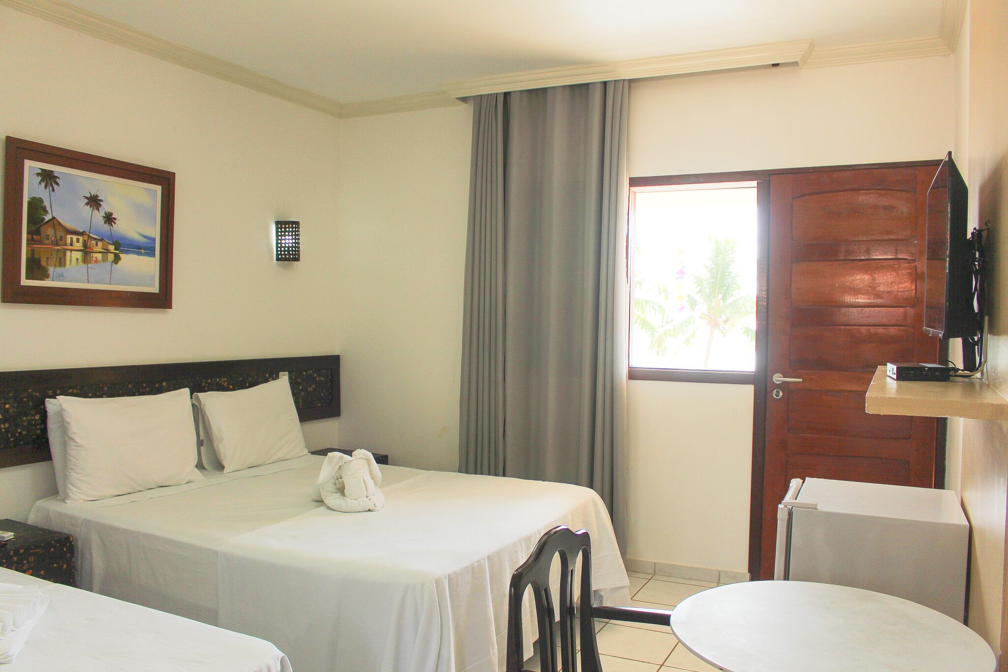Une chambre d’hôtel avec un lit, une chaise, une petite table, un tableau au mur et une porte.
