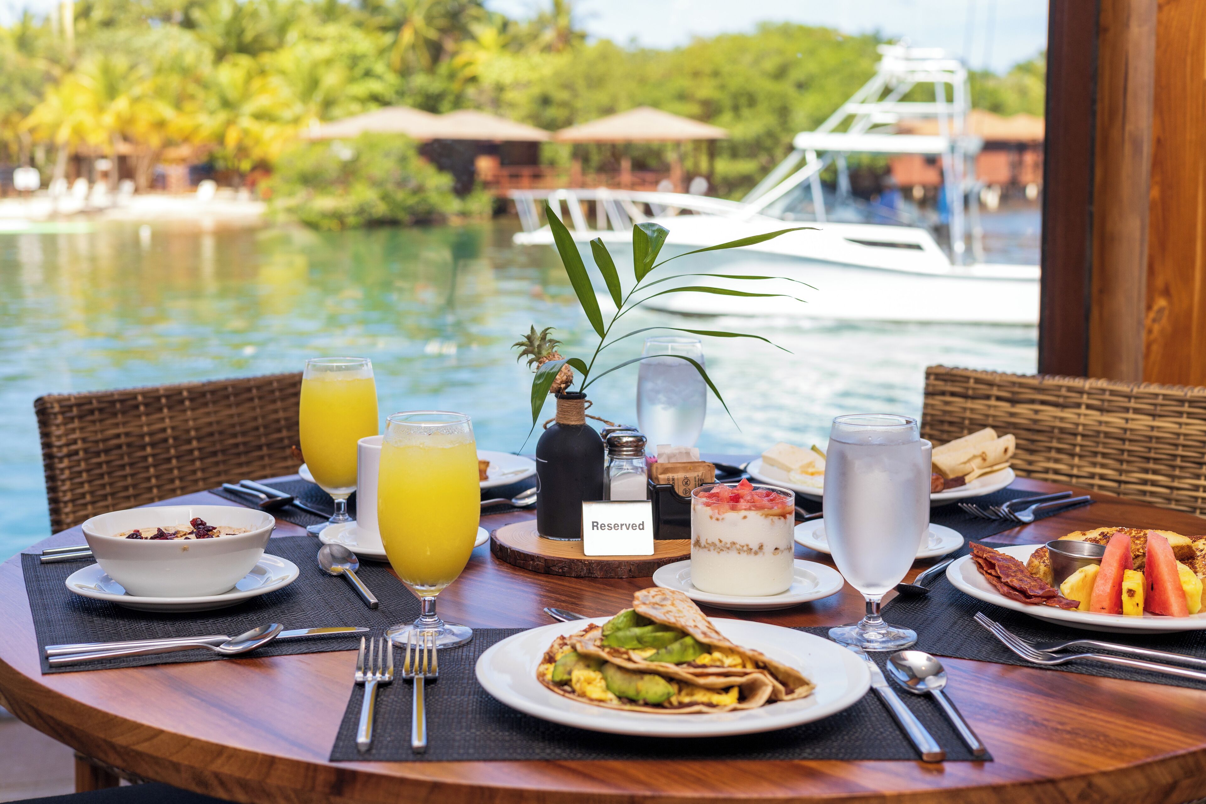 A table set with breakfast items, including a bowl of cereal, a glass of orange juice, and a plate of eggs and avocado.