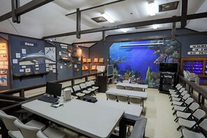 A classroom with tables, chairs, a projector, and an aquarium wall.