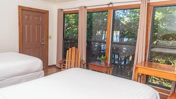Una habitación con dos camas, una silla de madera, una mesita pequeña y ventanas grandes con cortinas.