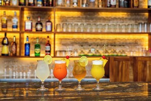 A bar with four cocktails, each garnished with a lime and a cherry, and a variety of bottles in the background.