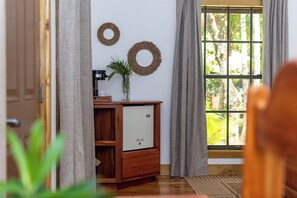 A room with a wooden cabinet, a small refrigerator, a potted plant, and a window with curtains.