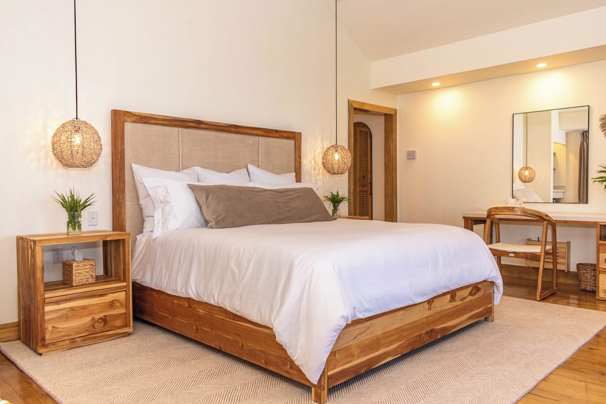 A bedroom with a wooden bed, two bedside tables, a nightstand, a mirror, and a desk with a chair.