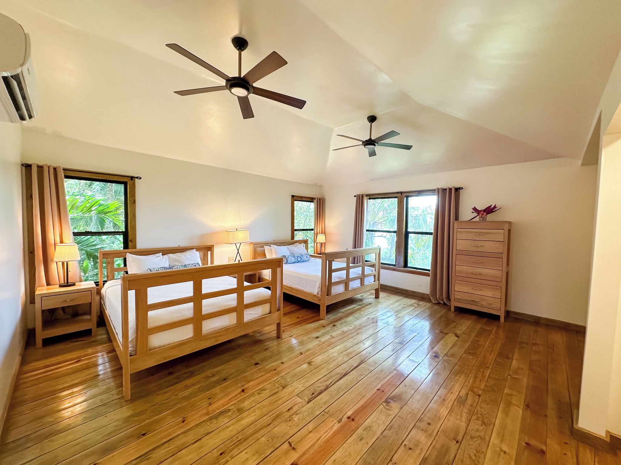 A spacious bedroom with wooden flooring, two single beds, a wooden dresser, and two ceiling fans.