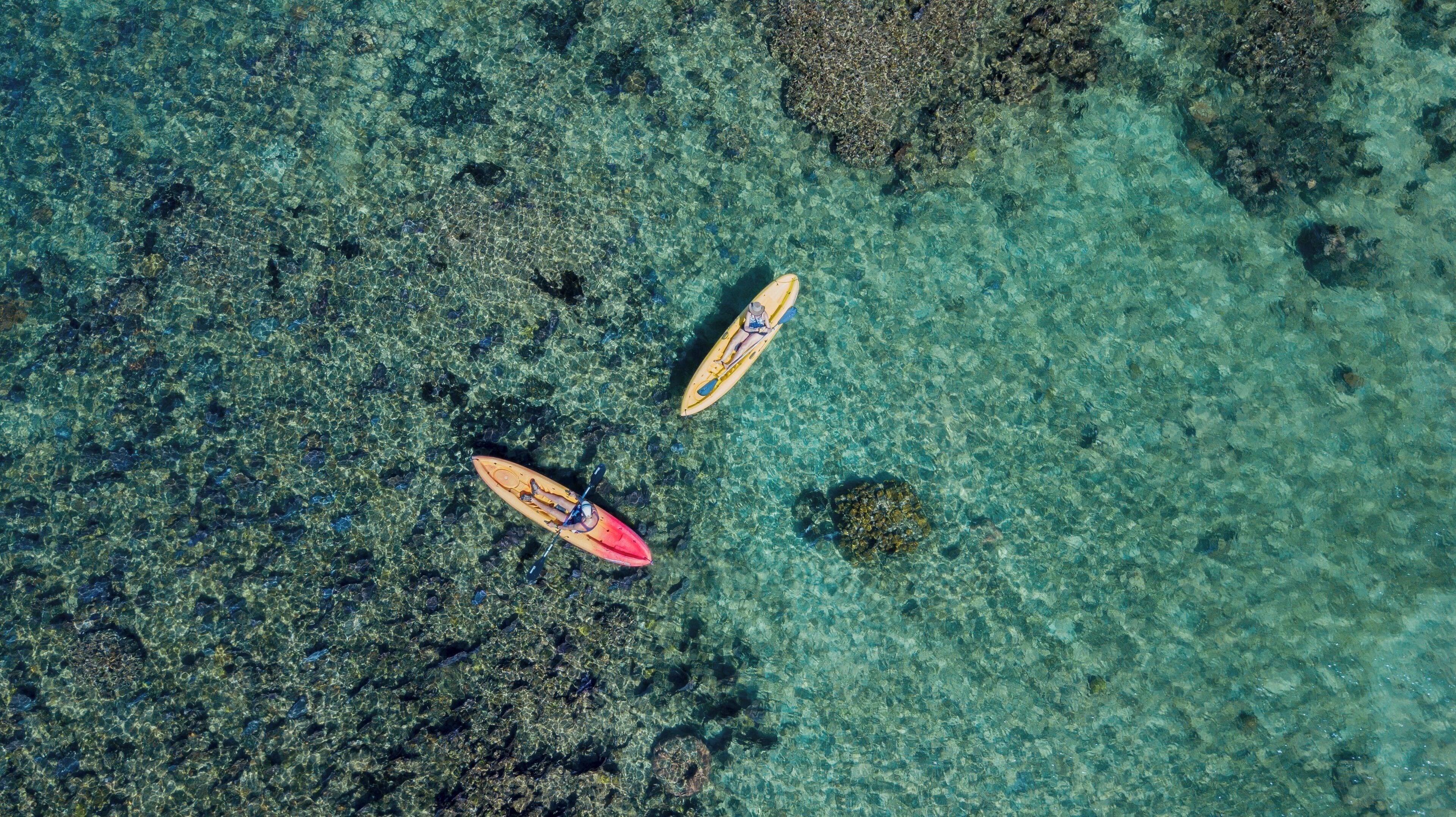 Kayak flotant en aigües clares i poc profundes, on es veuen roques i formacions corallines sota la superfície.