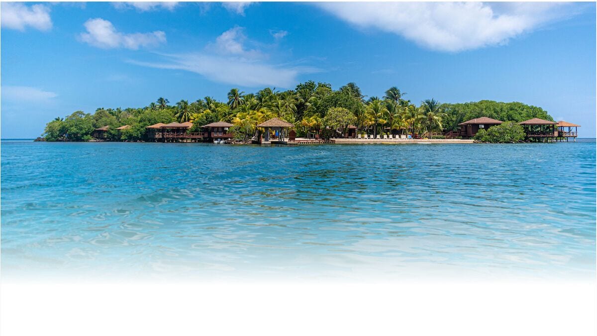 Un complexe hôtelier de style tropical situé sur une île, avec des bungalows sur pilotis, une eau d’un bleu cristallin et une végétation luxuriante.