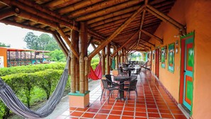 Espaço ao ar livre coberto com pilares de bambu, piso de azulejos e assentos externos.