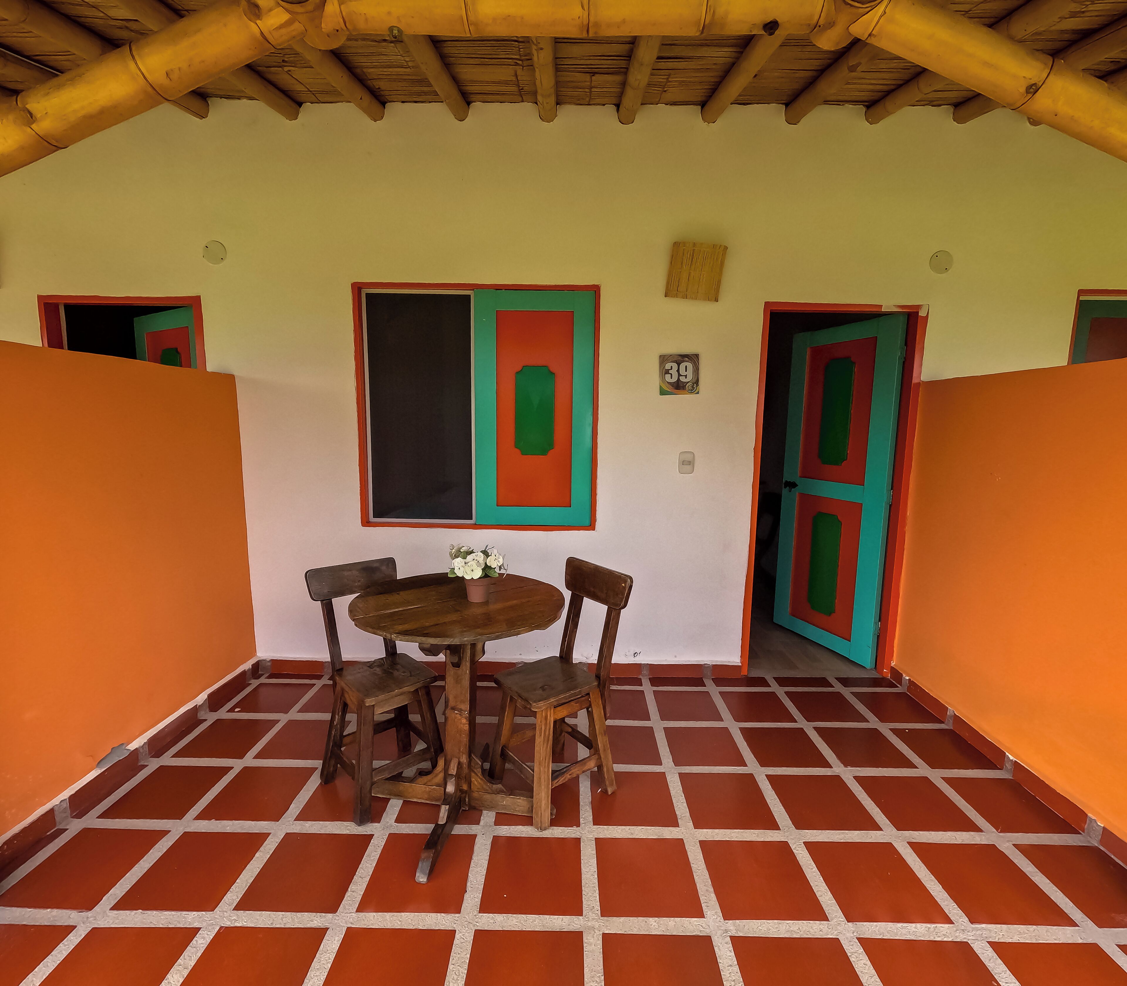 A room with a tiled floor, a wooden table with four chairs, and two doors with colorful frames.