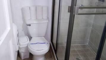 Ein kleines Badezimmer mit Toilette, Duschkabine und Ablage über der Toilette.