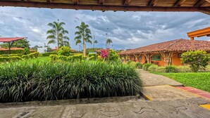 Uma trilha leva a um edifício com telhado de telhas, cercado por vegetação exuberante e palmeiras.