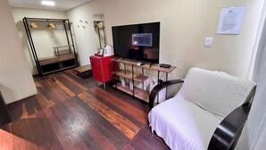 A compact living space with a flat-screen TV, a red mini-fridge, a sofa, and a wooden floor.