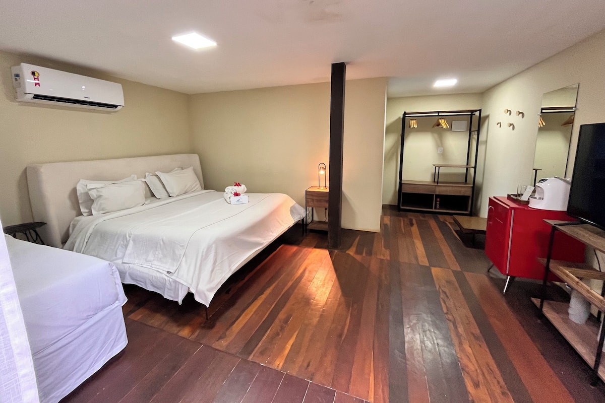 A hotel room with a bed, a desk, a TV, and an air conditioning unit.