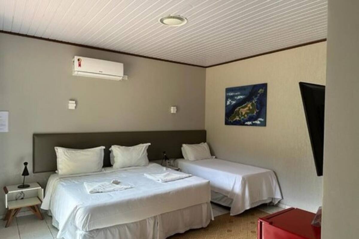 A hotel room with two beds, a ceiling fan, an air conditioning unit, a small table with a lamp, and a painting on the wall.