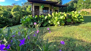 A house with a porch, surrounded by lush greenery and flowering plants.