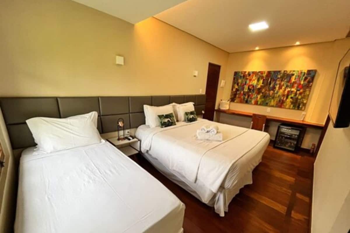 A hotel room with two beds, a nightstand, a painting on the wall, and a wooden floor.