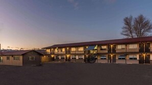 A multi-story motel with a red roof and multiple windows, featuring a covered outdoor seating area and a staircase leading to the upper levels.