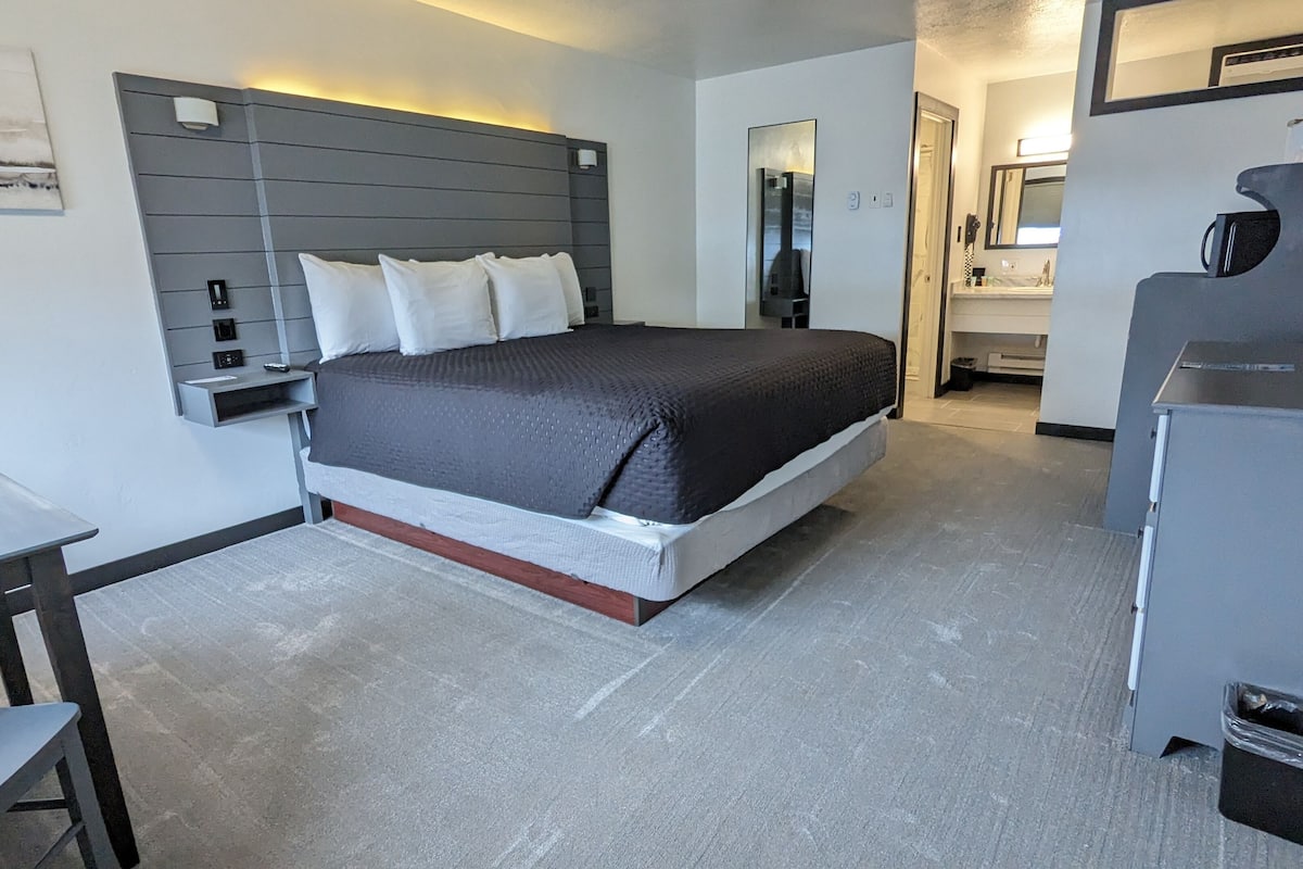 A modern hotel room with a bed, bedside table, and a small desk.