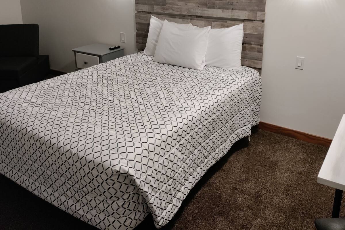 A neatly arranged bedroom with a wooden headboard, a patterned bedspread, and three wall-mounted light fixtures.