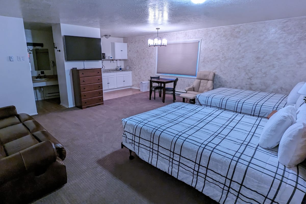 A compact room with two beds, a small dining area, a kitchenette, and a seating area.