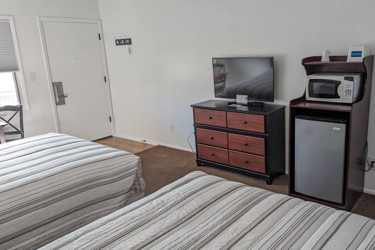 A hotel room with two beds, a dresser, a television, a microwave, and a refrigerator.