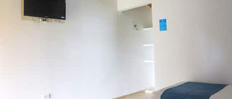 A room with a flat-screen TV mounted on the wall, a bed with a blue blanket, and a white wall with a small blue sign.