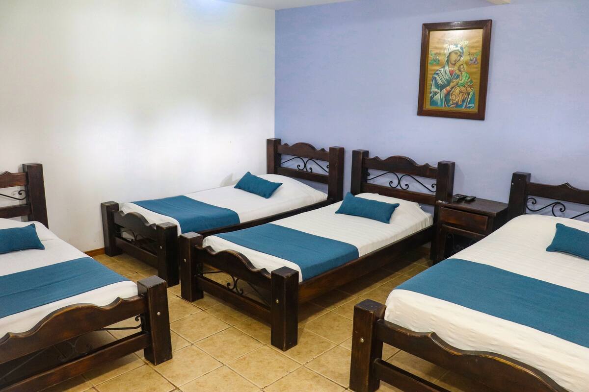 Une chambre d’hôtel avec quatre lits en bois, chacun doté de draps bleus et d’une tête de lit décorative.