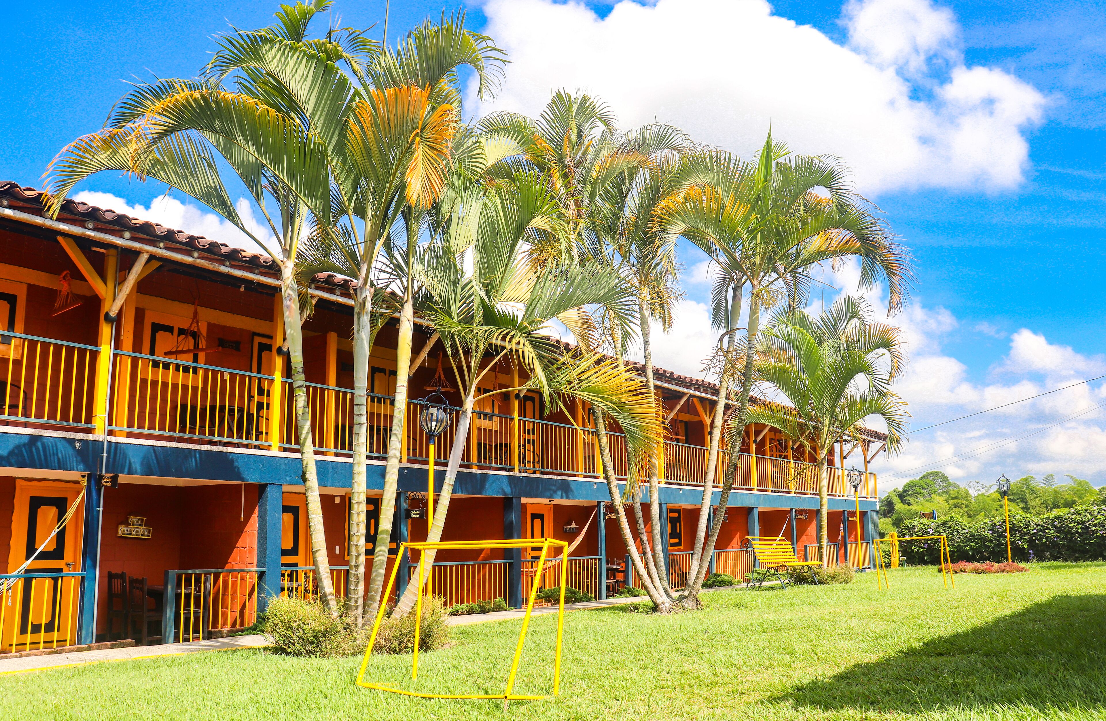 A two-story hotel with balconies, palm trees, and a grassy lawn.