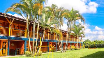 Un hotel de dos pisos con balcones, palmeras y un césped.