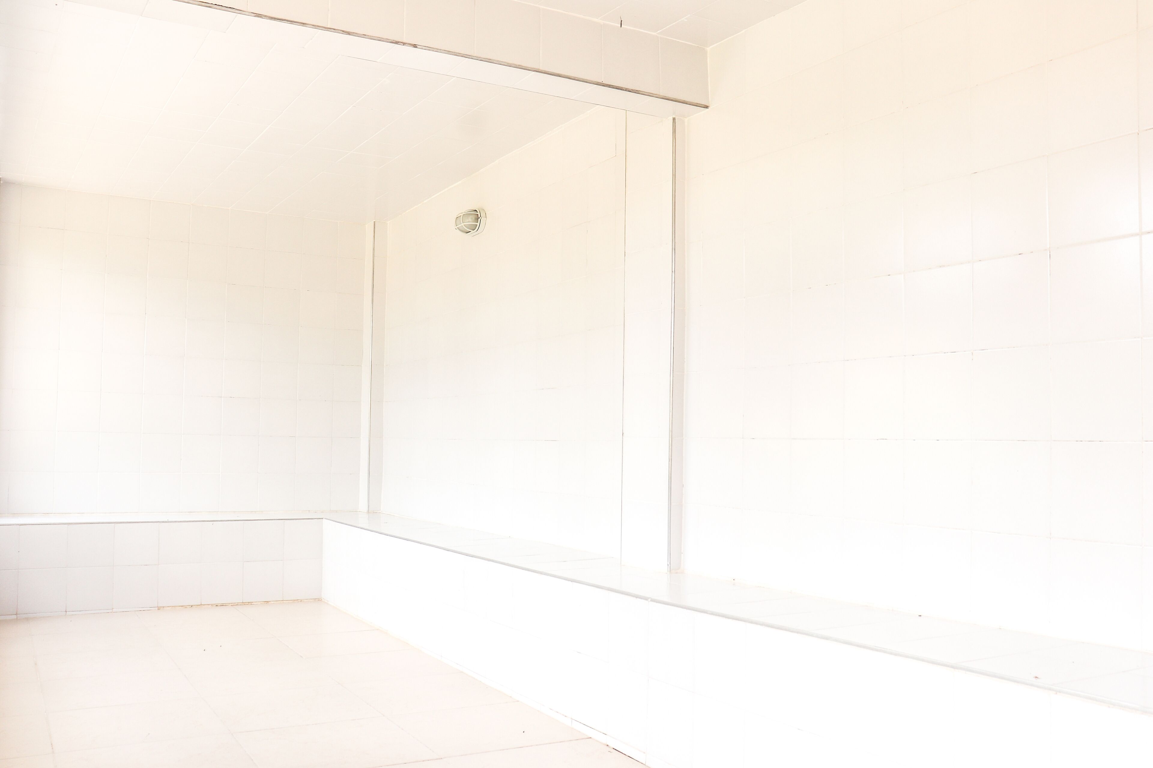 A bathroom with white tiles, a glass shower enclosure, and a visible drain.