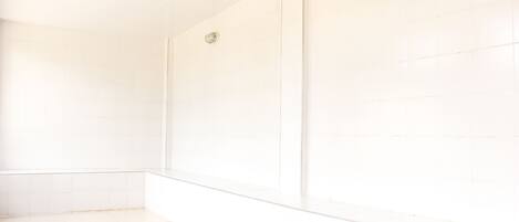 A bathroom with white tiles, a glass shower enclosure, and a visible drain.