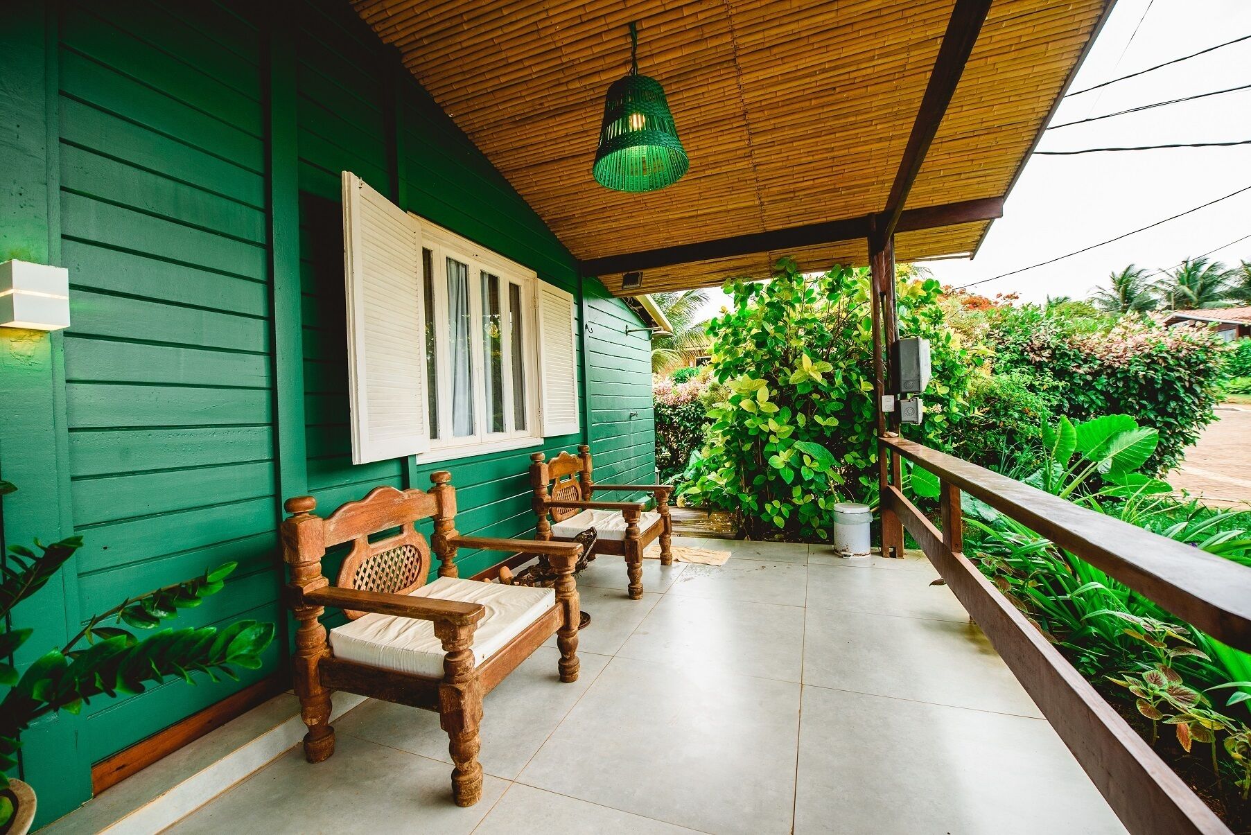 A porch with two wooden chairs and a bench, a green wall, and a wooden ceiling.