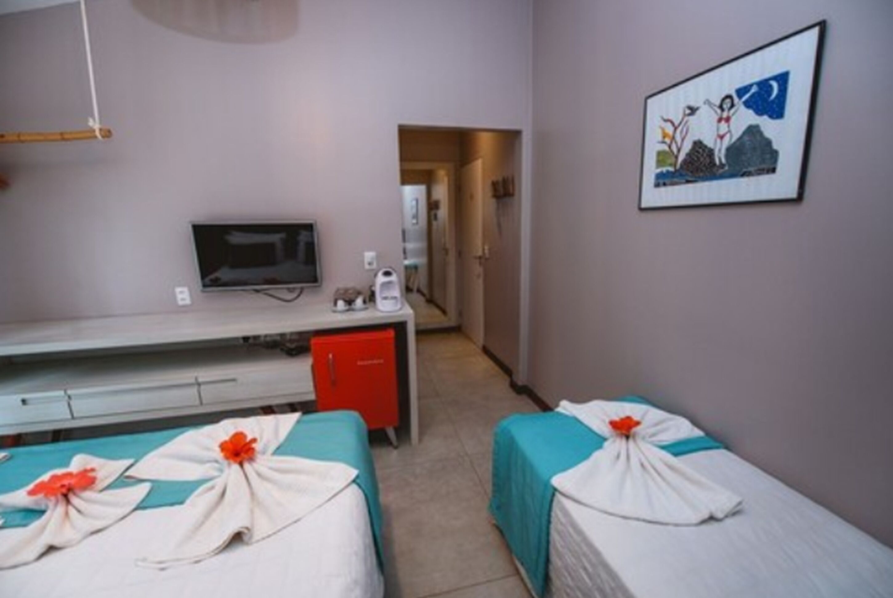 A hotel room with two beds, a desk with a television, and a small kitchenette.