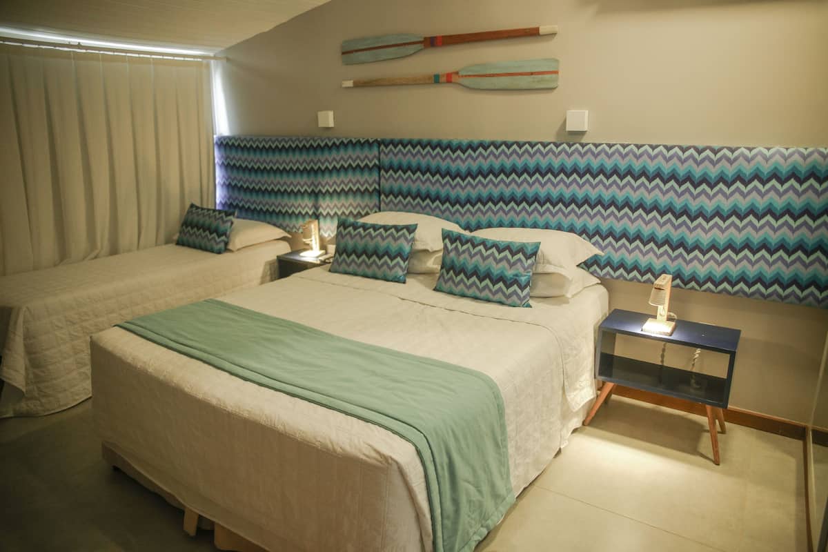 A hotel room with two beds, a nightstand, a wall-mounted shelf, and a window with curtains.