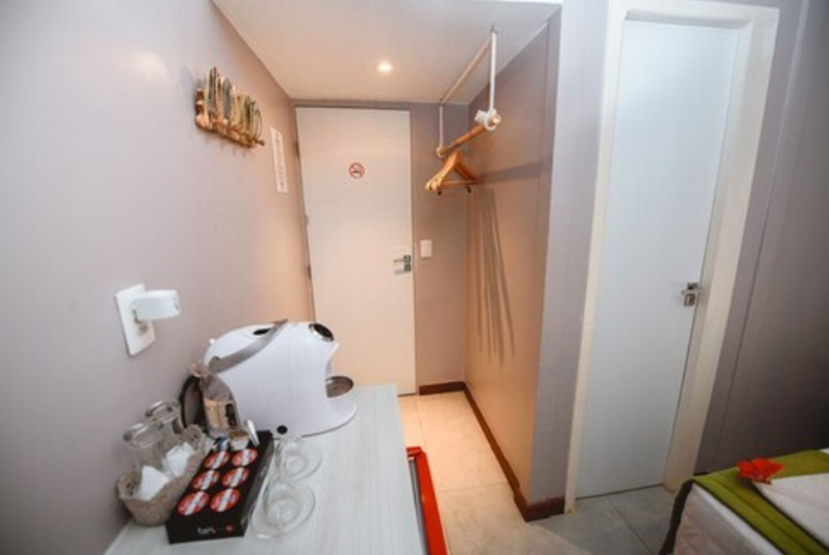 A compact hotel room with a kitchenette, a shower area, and a bed with a green bedspread.