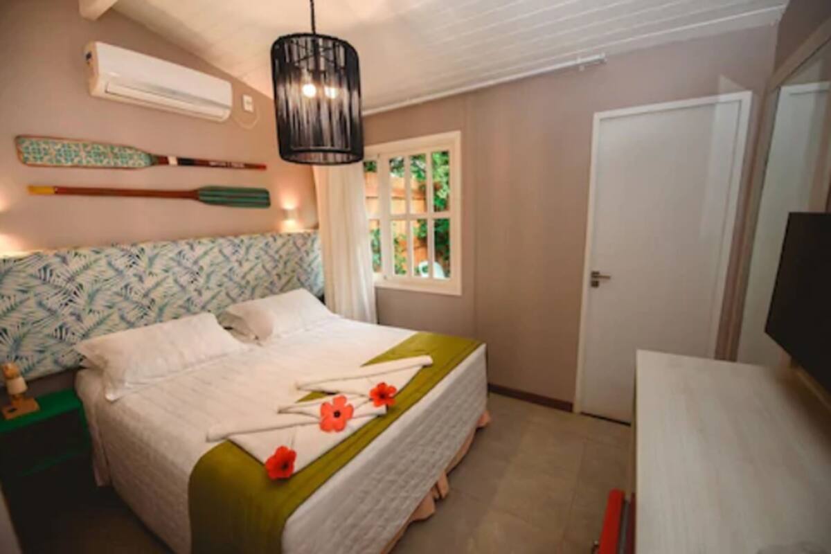 A neatly arranged bedroom with a bed, a bedside table, a TV, and a window with curtains.
