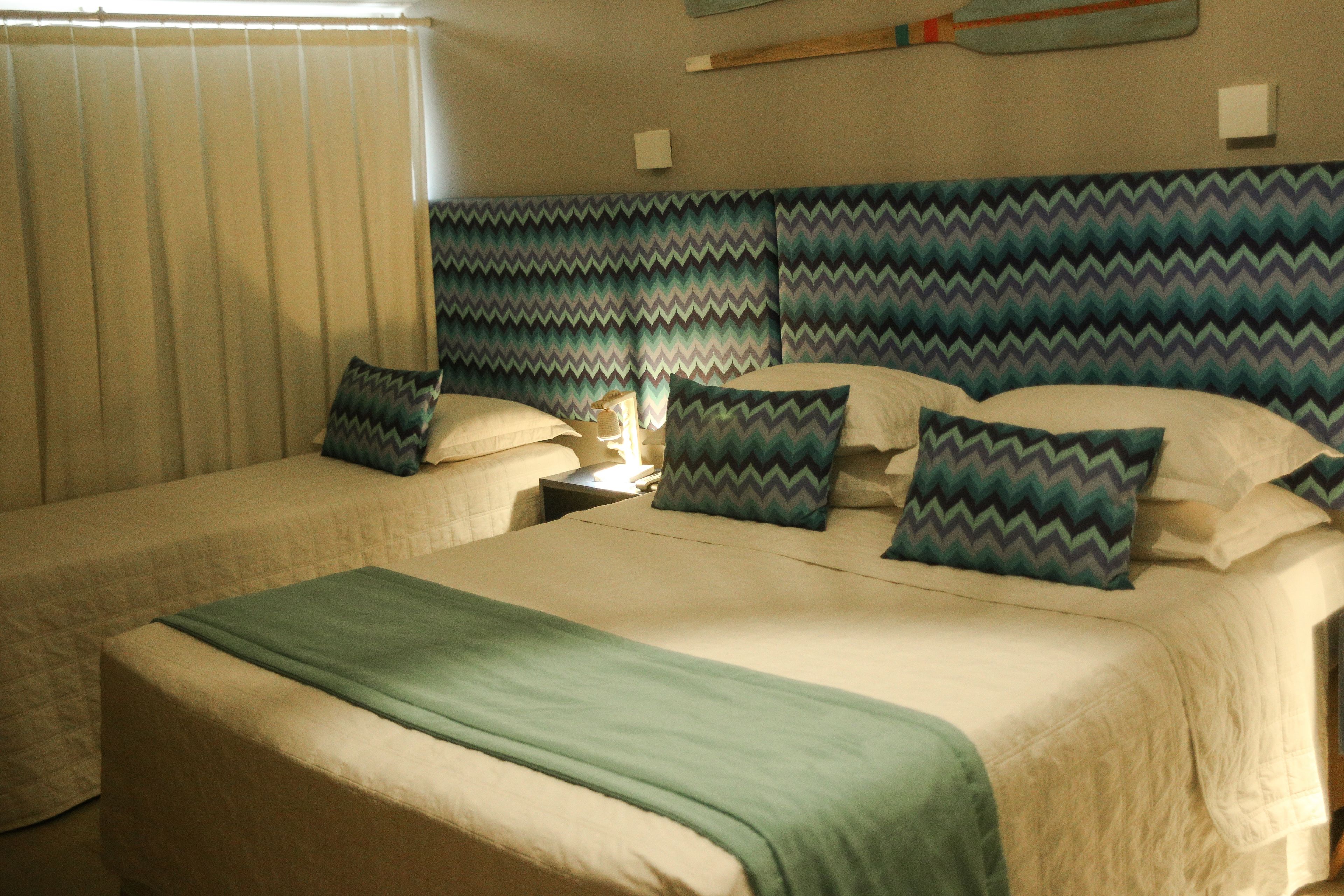 A hotel room with two beds, a headboard with a zigzag pattern, and a window with blinds.