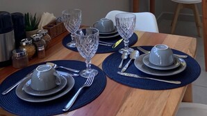 A dining area with a table set for two, featuring clear glassware and silverware, a small potted plant, and a view of greenery through the window. - Pousada da Mana (Fernando de Noronha)