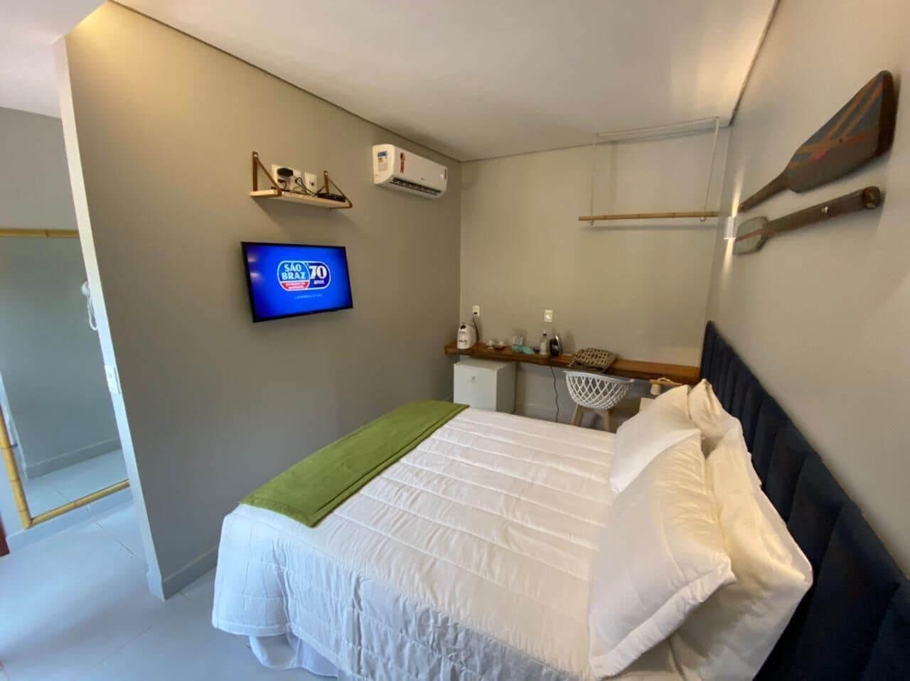 Habitación de hotel con cama, televisión, aire acondicionado y repisas con artículos de aseo.