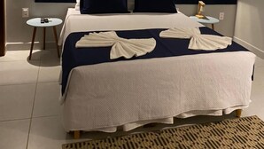 A neatly arranged hotel room with a large bed, two bedside tables, a wall-mounted air conditioner, and a framed artwork above the bed. - Pousada da Mana (Fernando de Noronha)