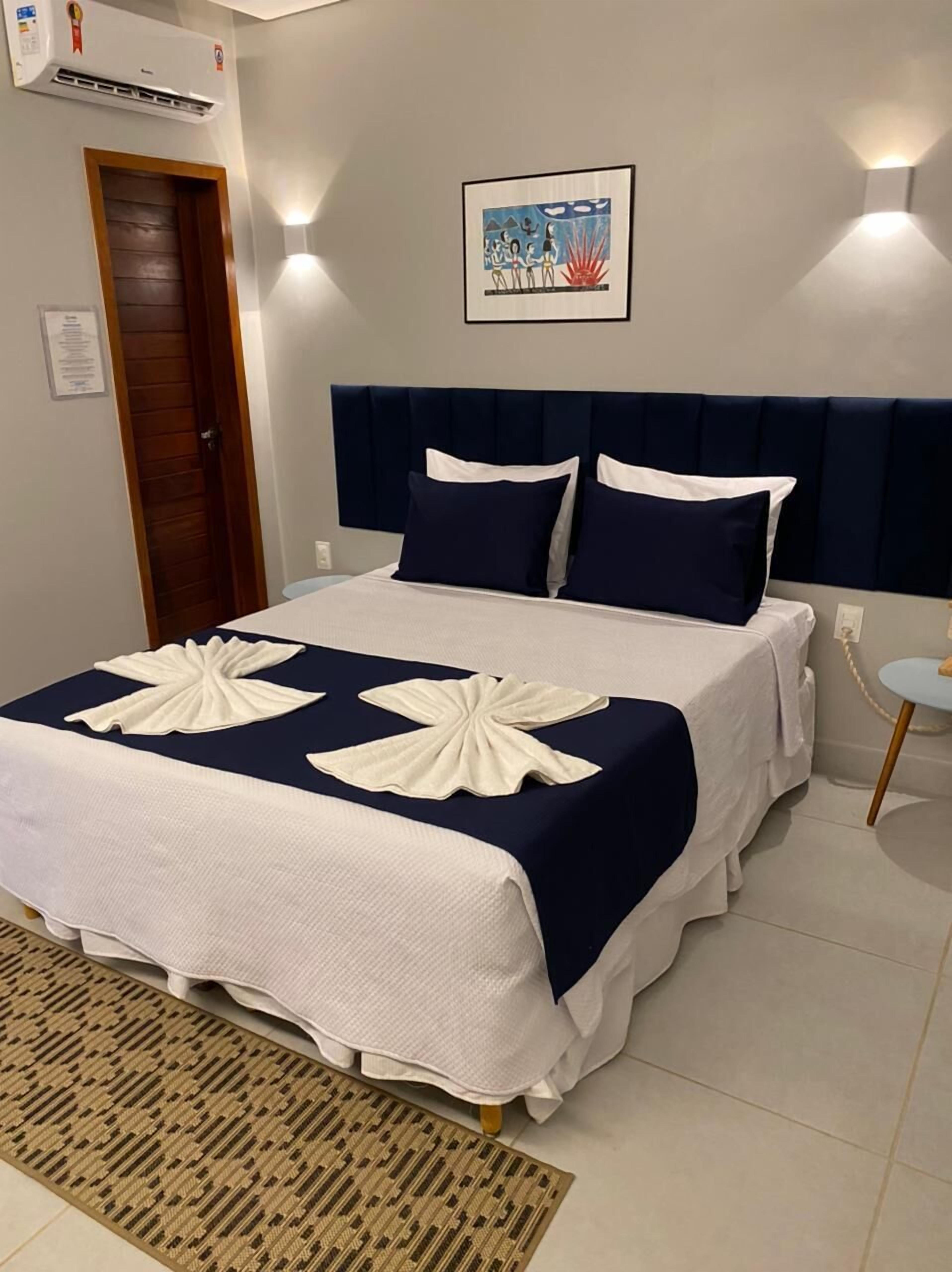 A neatly made bed with a dark headboard and white bedding, a framed picture on the wall, and a door to the left.
