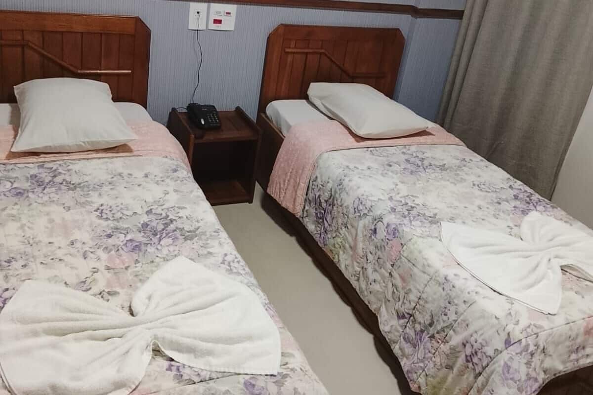 Une chambre d’hôtel avec deux lits, chacun agrémenté de draps et de serviettes à motifs floraux. Une table de chevet avec un téléphone et une prise électrique se trouve entre les deux lits.