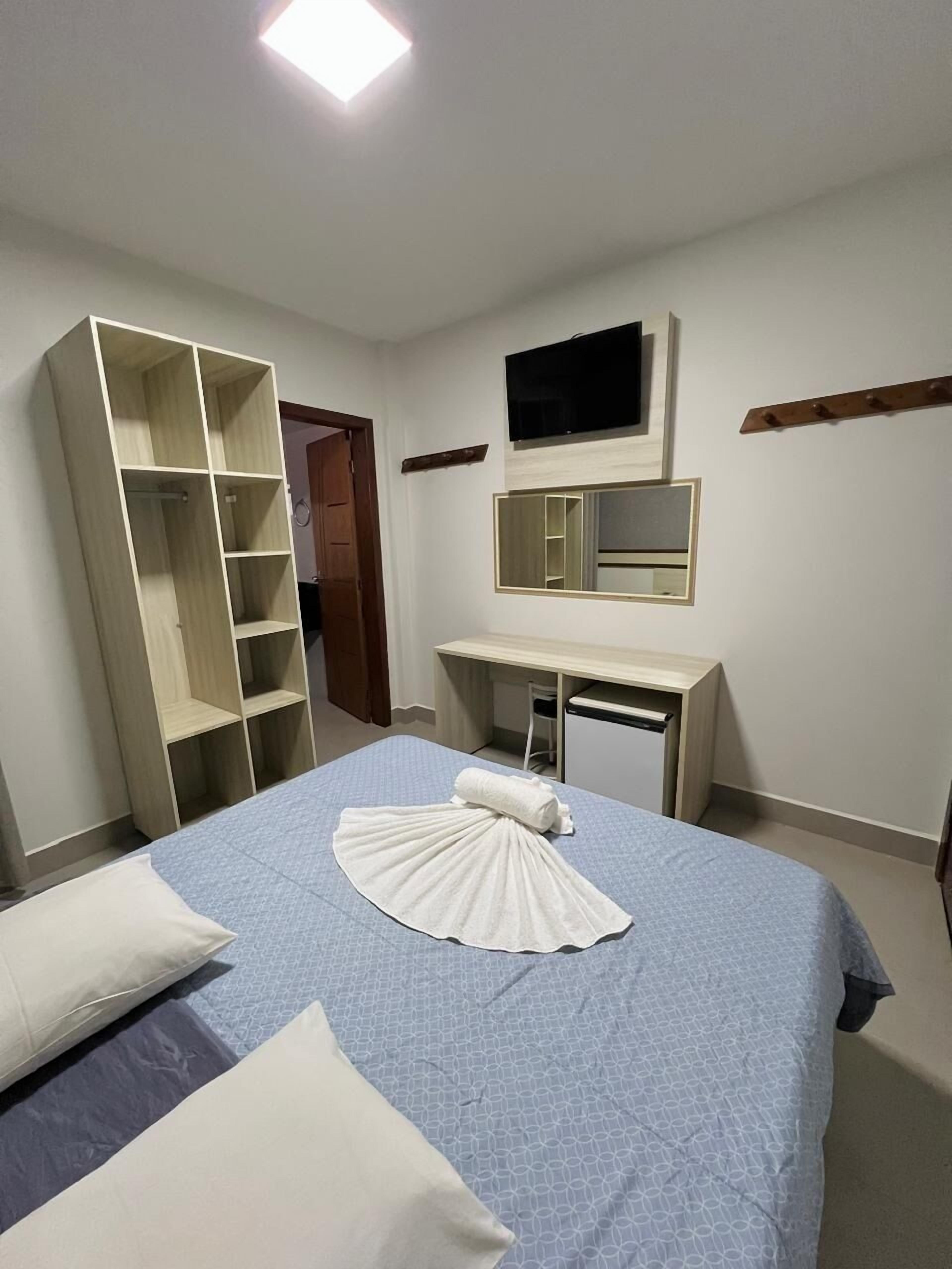 A hotel room with a bed, a desk, a TV, and a wardrobe.