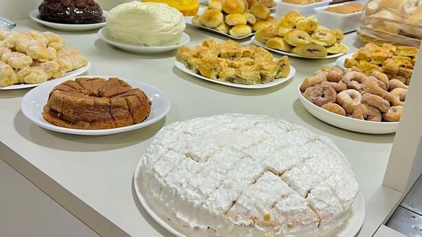 Buffet com diversos doces e pastelaria, incluindo bolos, biscoitos e salgados, expostos numa vitrine de vidro.