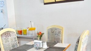 Un comedor con una mesa, sillas, un cuadro de fruta en la pared y un dispensador de jugo.
