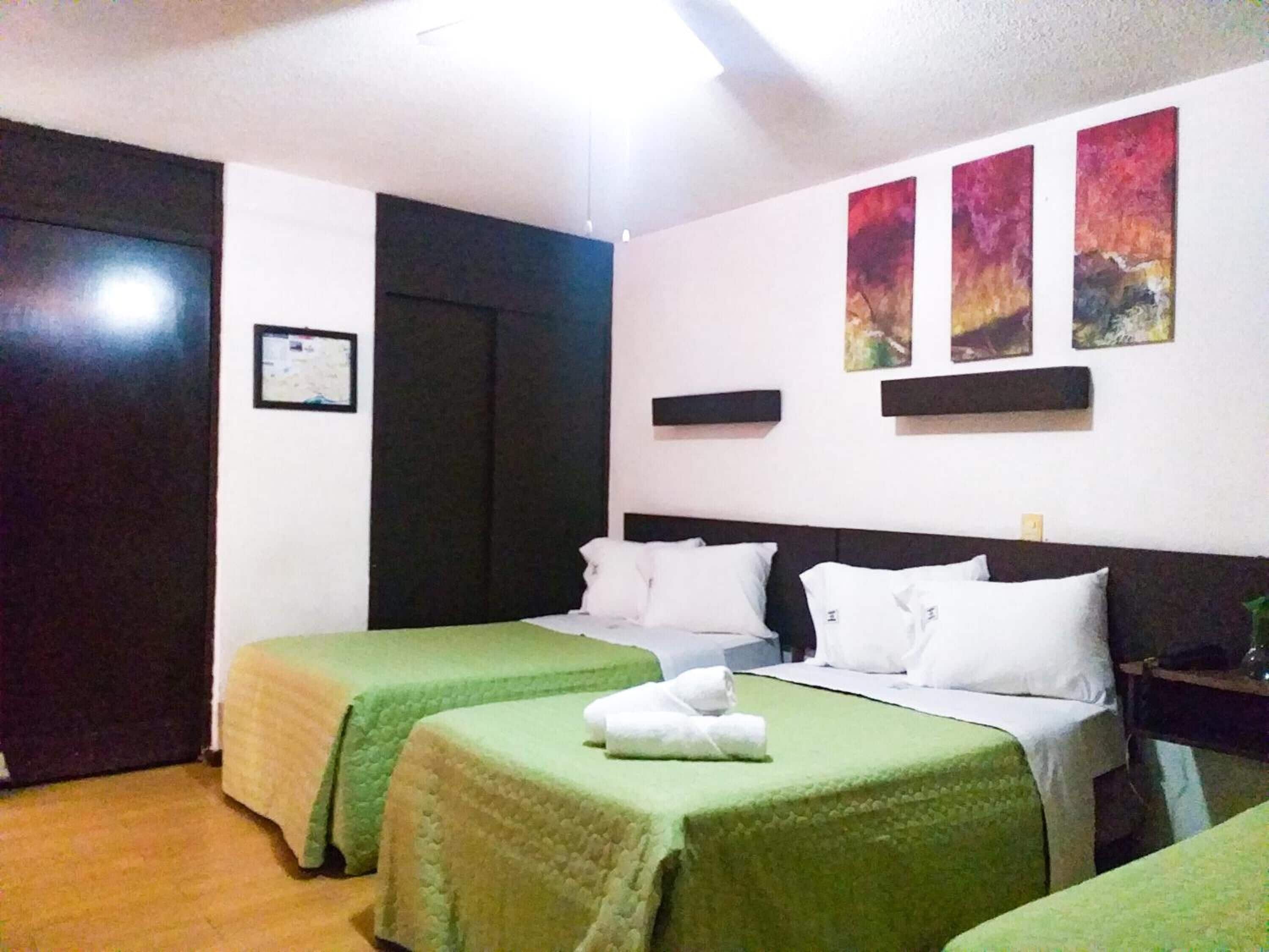 A hotel room with two single beds, a wooden floor, a dark-colored headboard, and three abstract paintings on the wall.