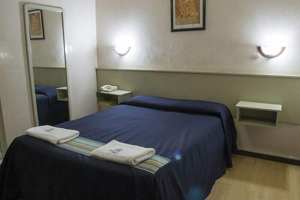 A hotel room with two beds, a bedside table with a phone, a mirror, and a wall-mounted light fixture.