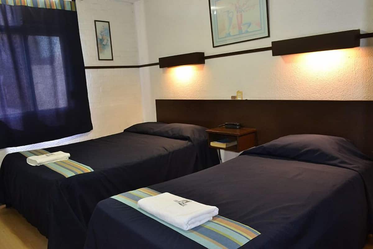 A hotel room with two single beds, a nightstand, a lamp, and a framed picture on the wall.