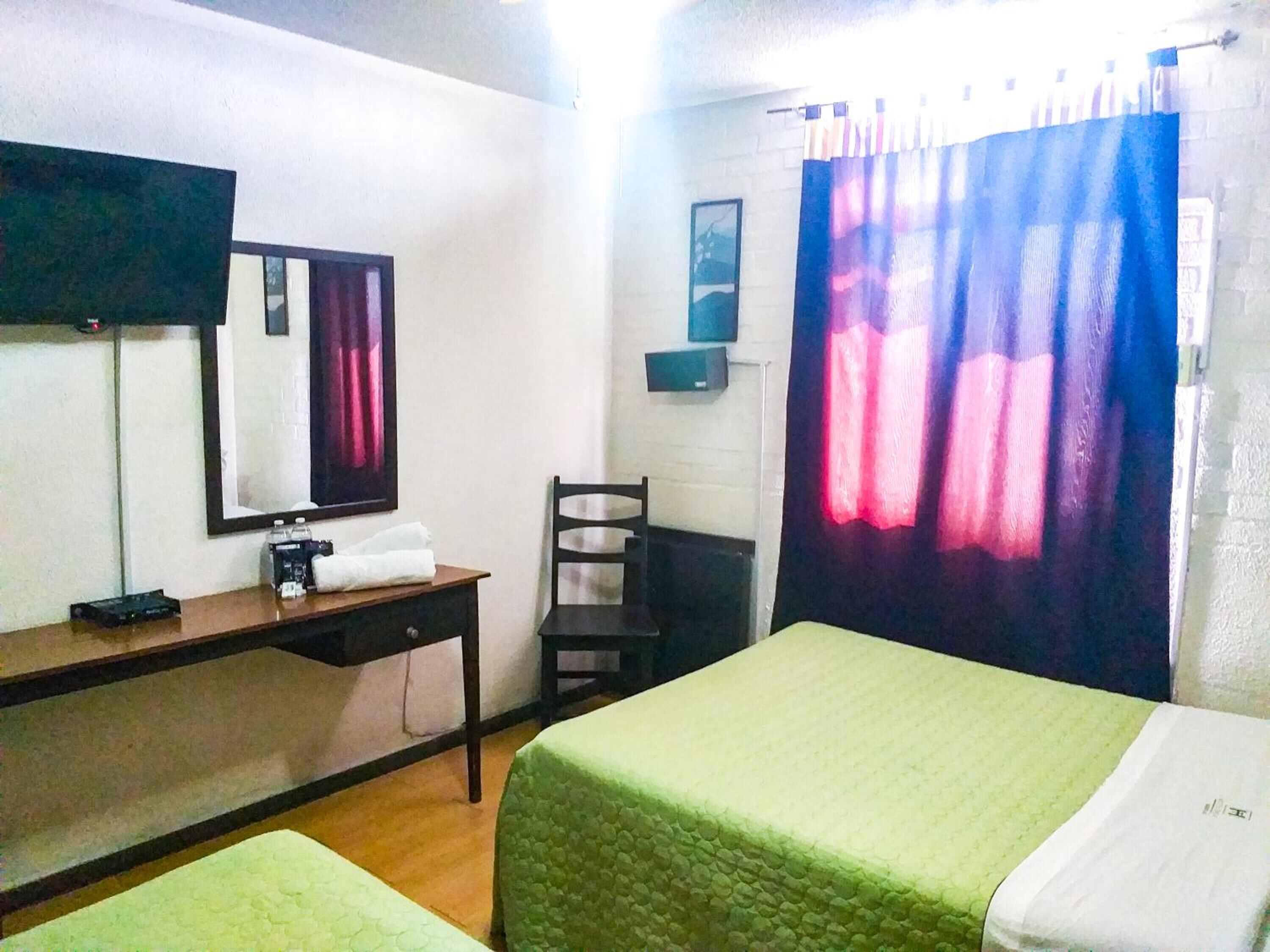 Una habitación de hotel con cama, escritorio, silla, televisor y cortina.