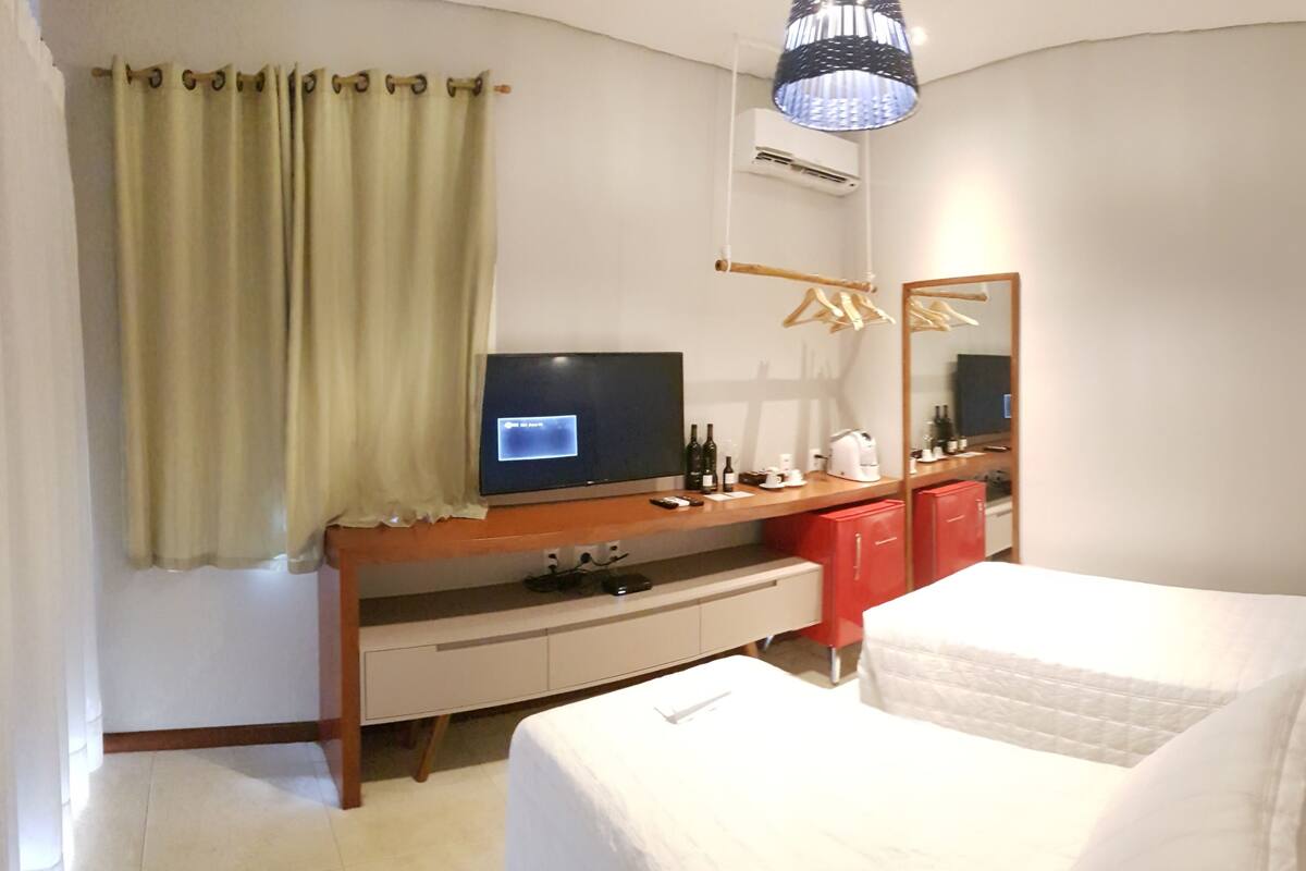 A hotel room with a bed, a TV on a wooden stand, a mirror, a wardrobe, and a hanging clothes rack.